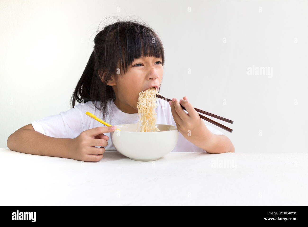 Portrait of Asian child girl eating instant noodles with white wooden table and white background. Stock Photo
