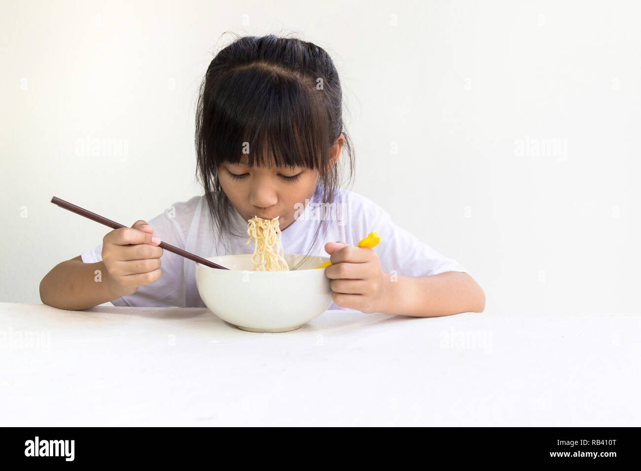 Portrait of Asian child girl eating instant noodles with white wooden table and white background. Stock Photo