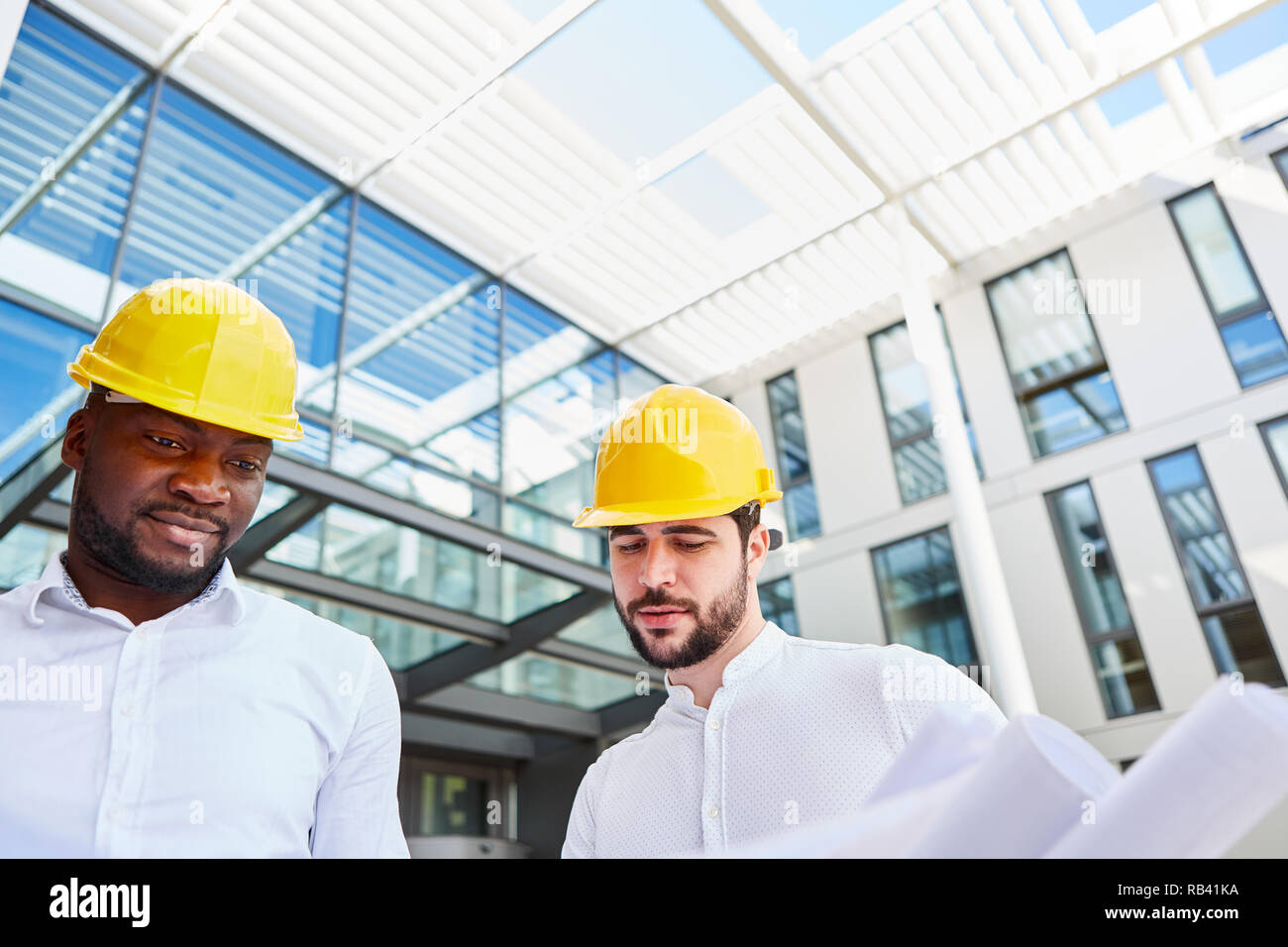Two business people as an architect with architectural drawing in front of an office building Stock Photo