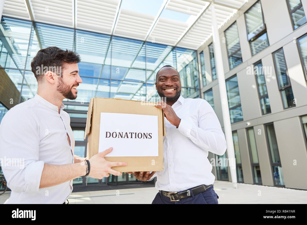 Two businessmen with a cardboard box as donation in kind symbolizing the common good Stock Photo