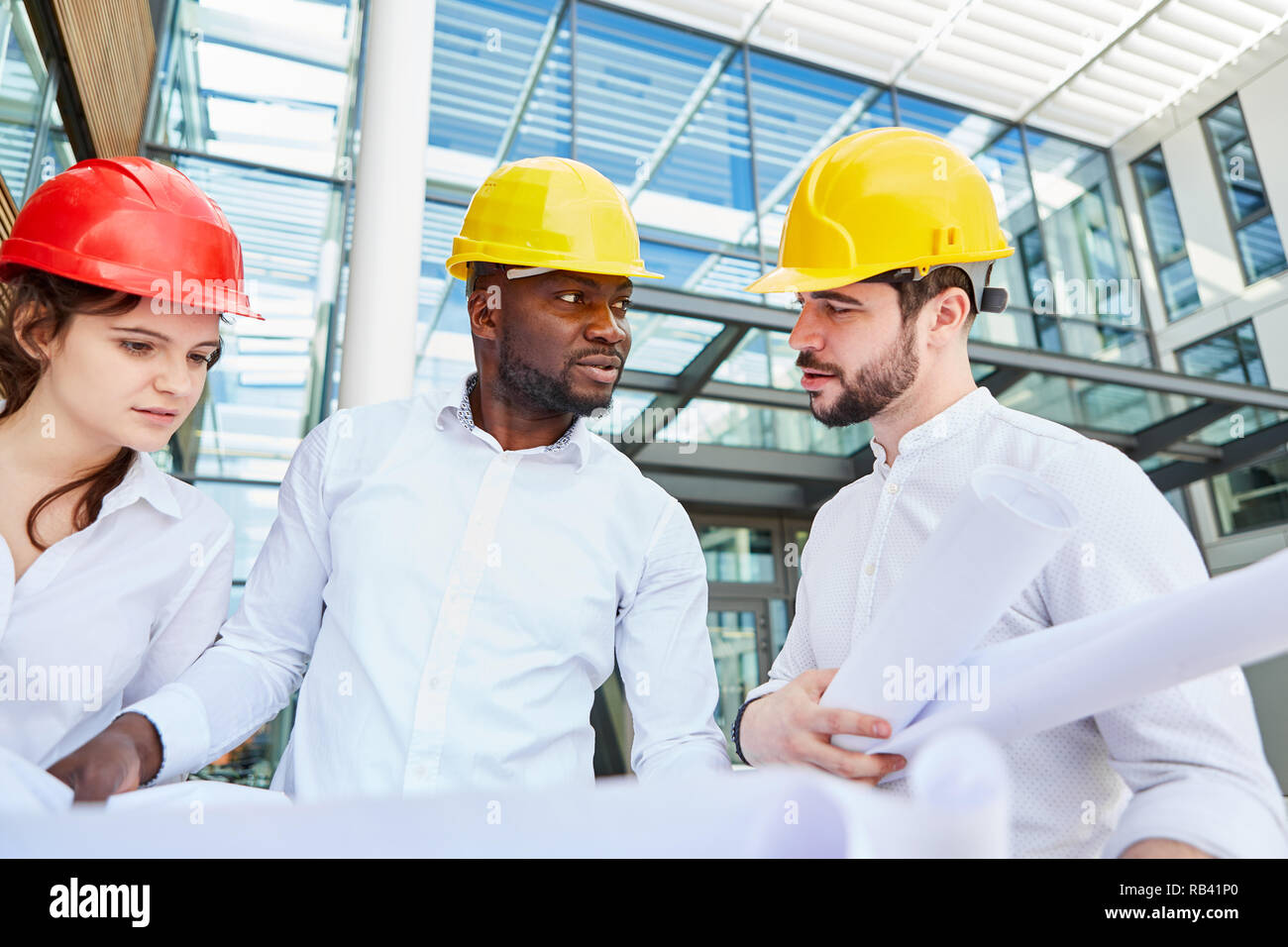 Construction manager holds construction drawings and talks to architect and engineer in front of office Stock Photo