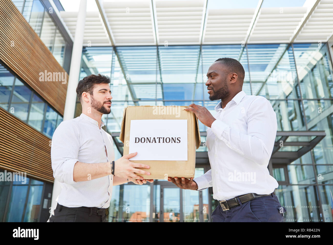 Two business people are holding a cardboard box labeled Donations Stock Photo