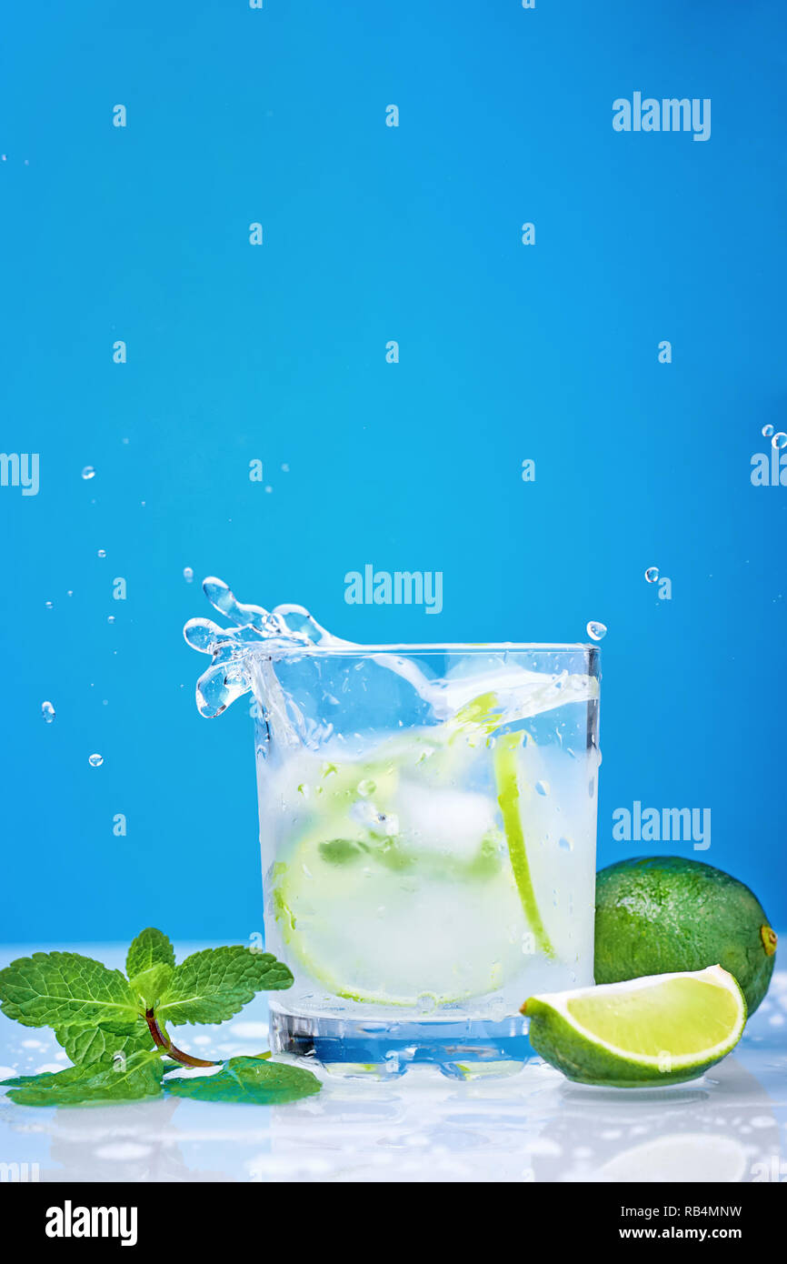 Splashing mojito cocktail with lime and fresh mint in glass on blue background Stock Photo