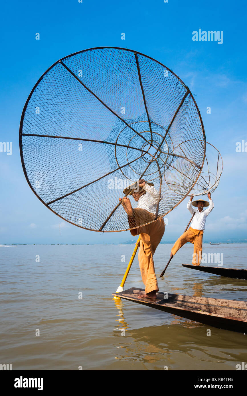 two fishermen in Inle Lake fishing in two boats in the traditional Burmese way with blue sky in the background Stock Photo