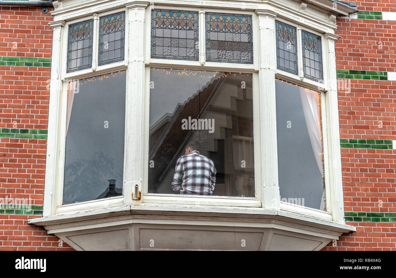 man sits with his back in front of the window inside a house Stock Photo