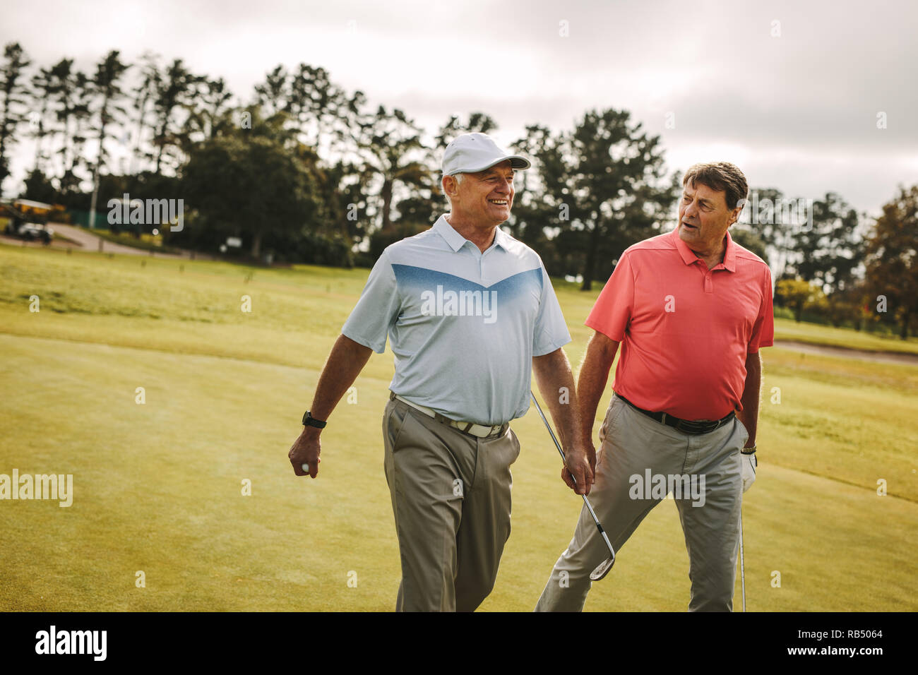 Two senior man playing golf are walking to the next hole. Professional golfers walking and talking on the golf course. Stock Photo