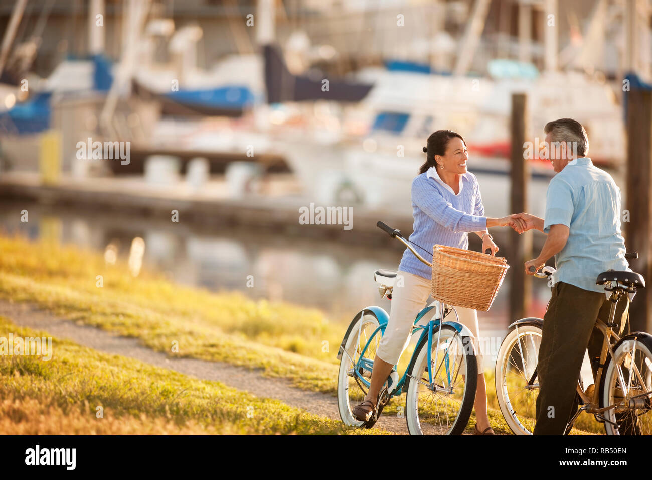 Middle Aged Couple Hold Hands And Look At Each Other While Riding Bicycles At A Boat Marina