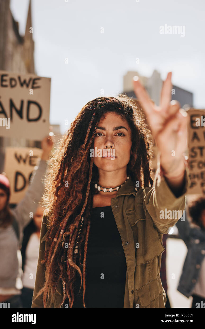 Female activist with peace sign at women's march. Woman leading a protest on road. Stock Photo