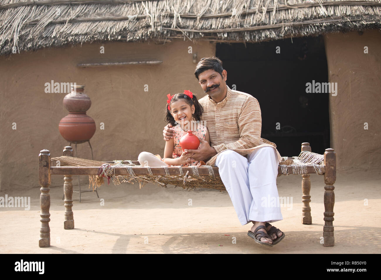 Indian father with daughter holding piggy bank while sitting on ...