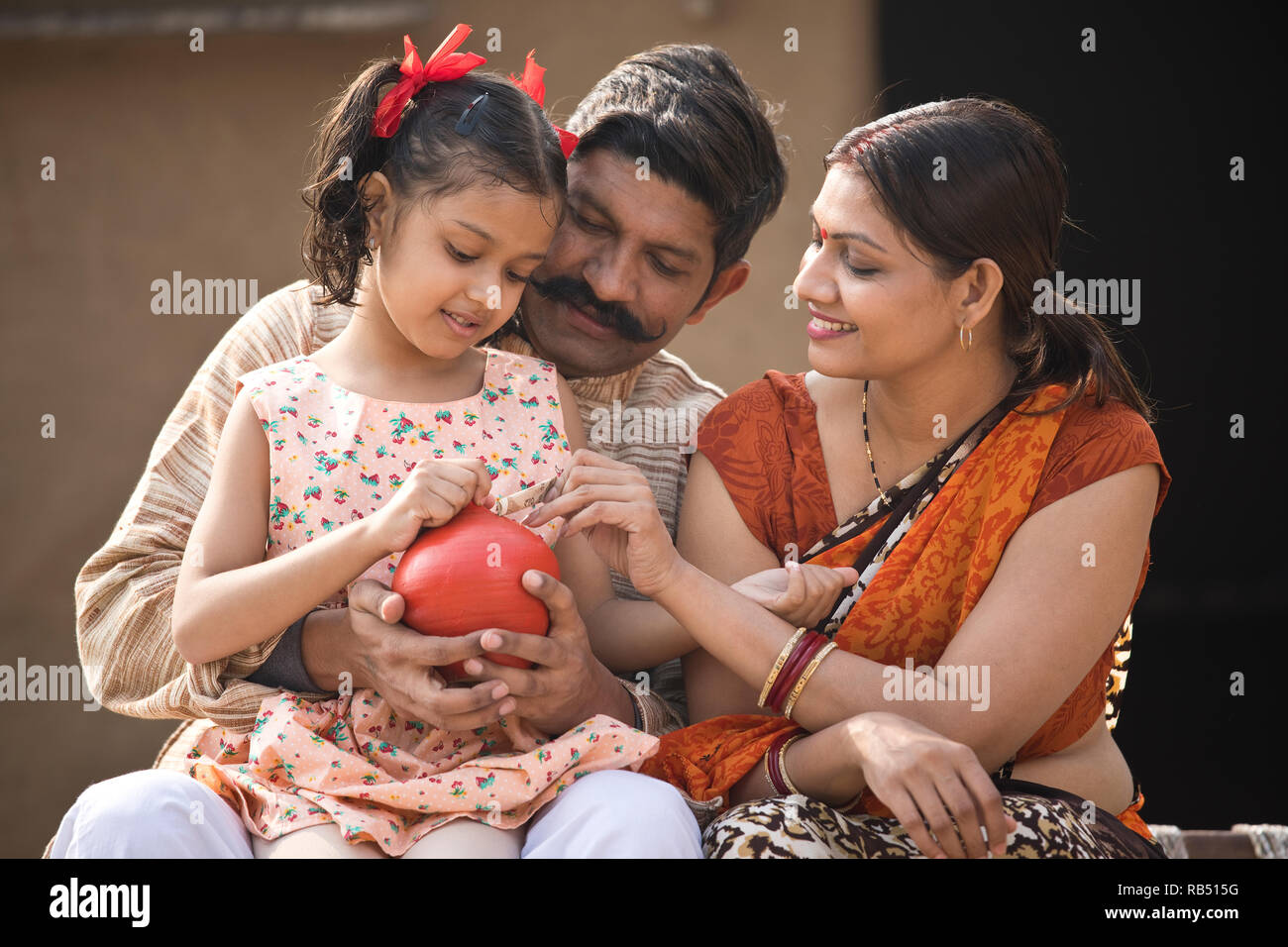 Indian parents with daughter holding piggy bank while sitting on ...