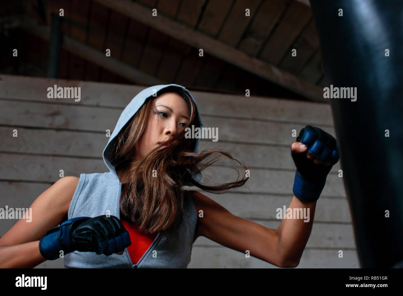 Tough young woman punching boxing bag. Stock Photo