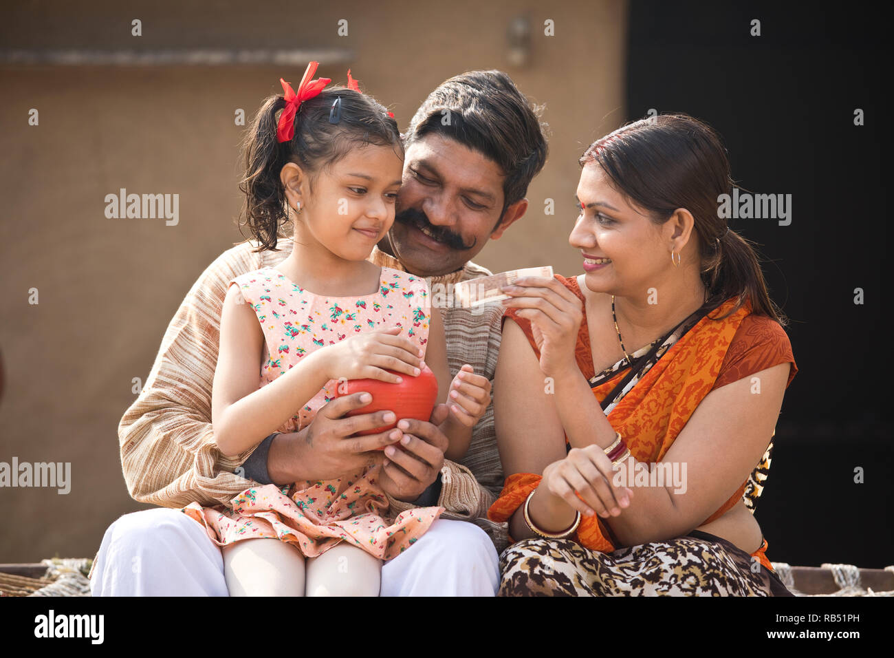 Indian parents with daughter holding piggy bank while sitting on ...