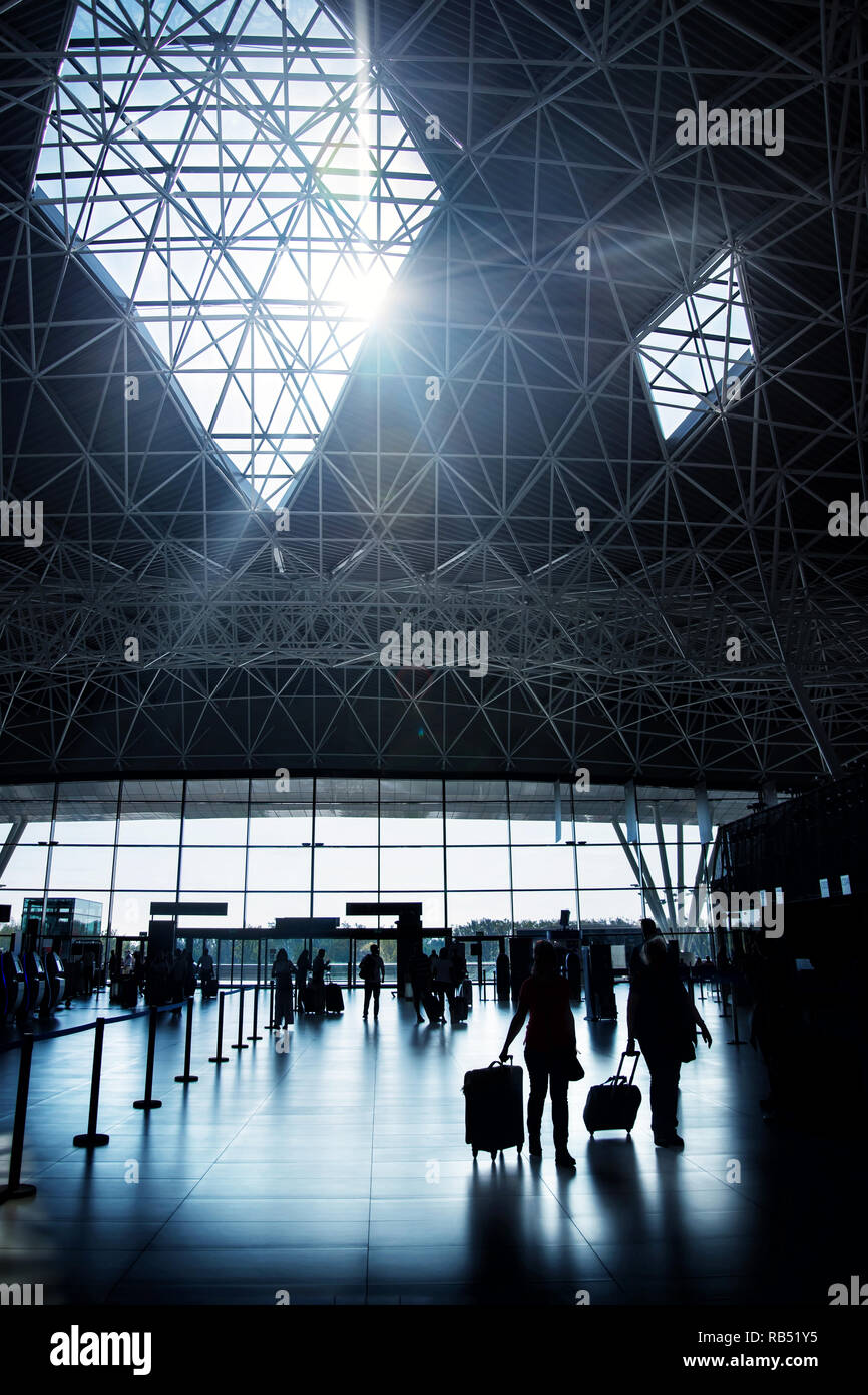 two women in silhouette walking towards check-in desk in Zagreb airport hall, Croatia, on sunny day with sun shining through roof window Stock Photo