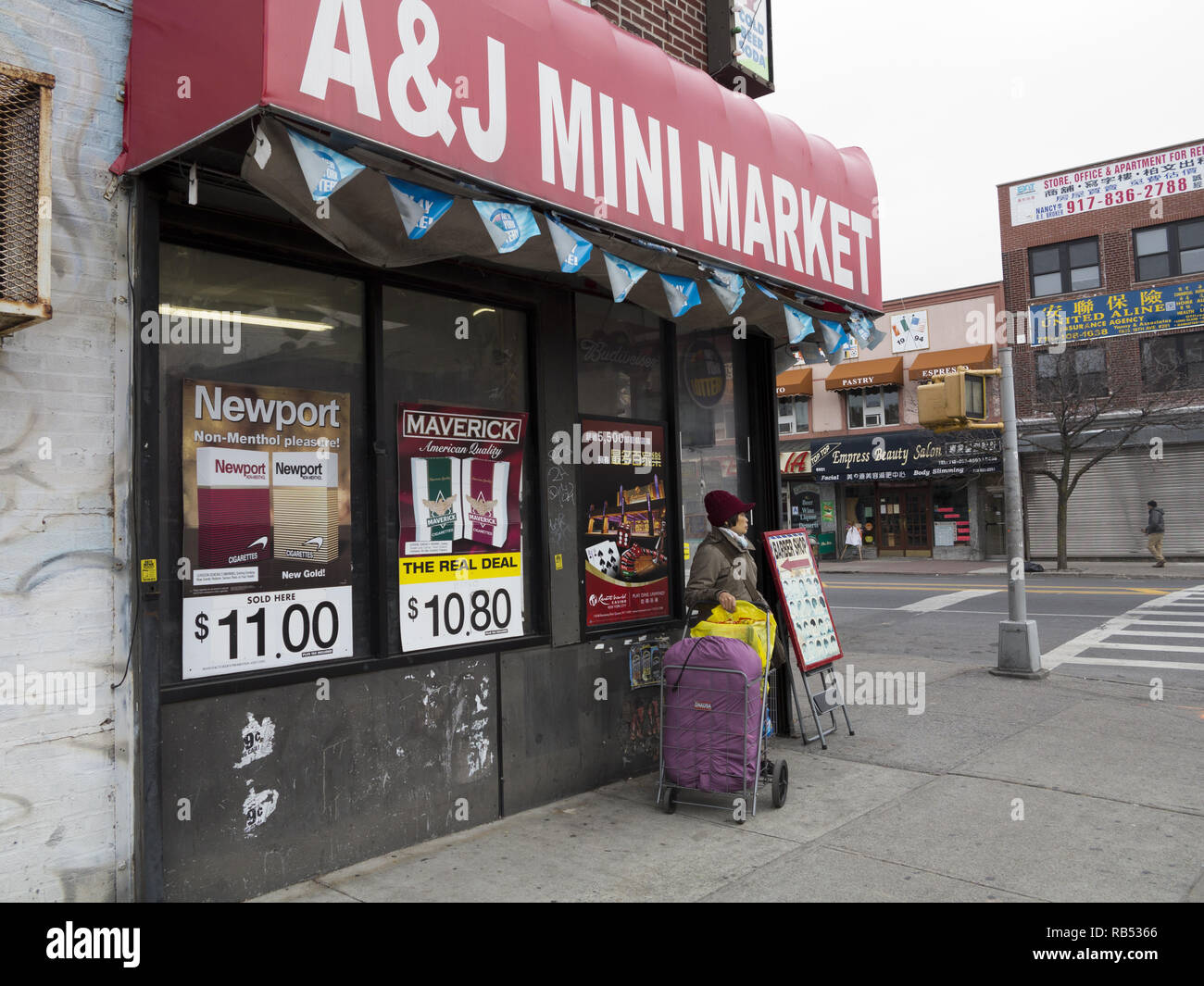 Chinese woman stands in front of mini market in the predominantly Chinese neighborhood of the Bensonhurst section of Brooklyn, NY. Cigarette ads and a Stock Photo