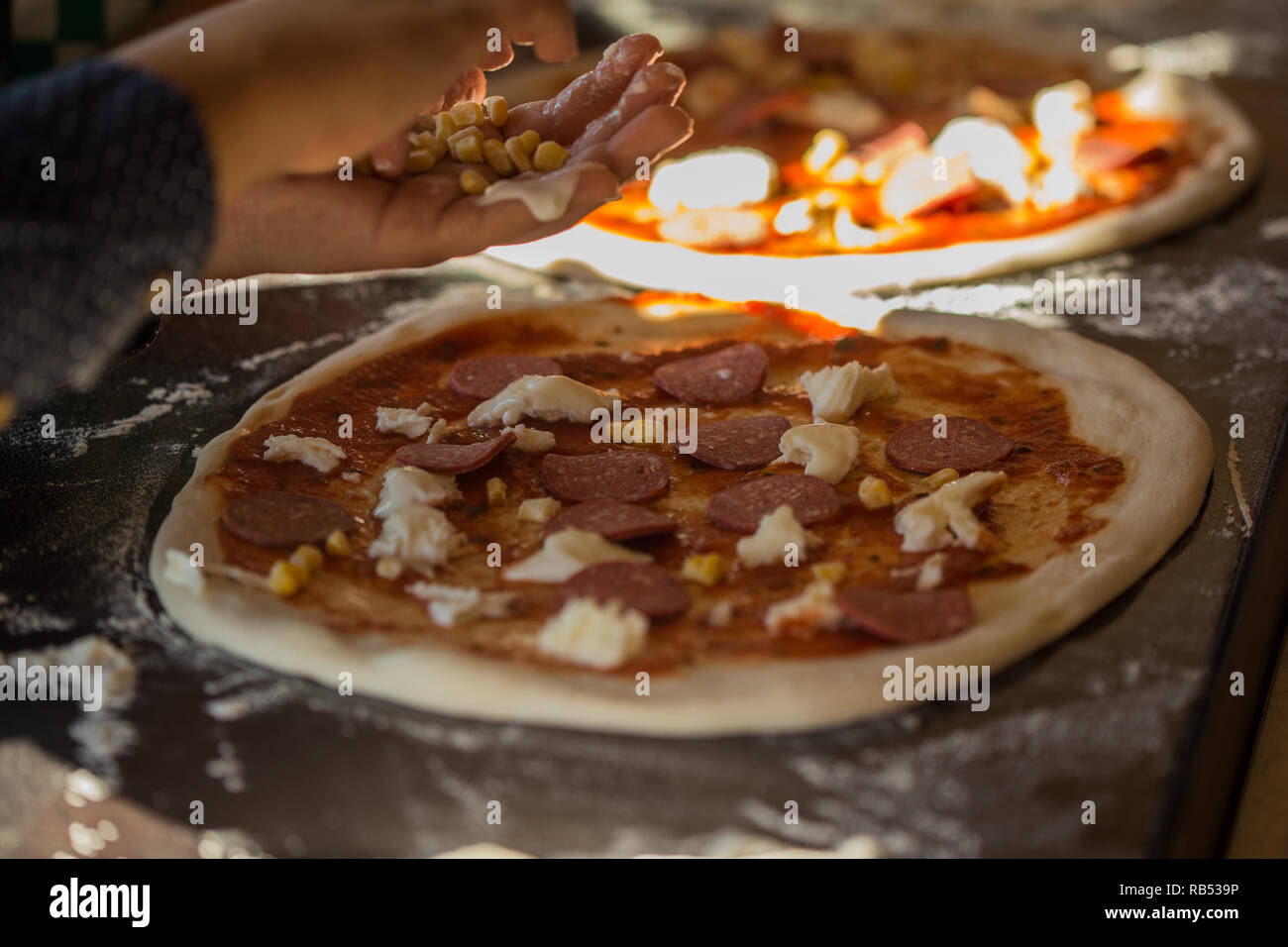 Pizza baking process. Child's hands putting corn on pizza with mozarella and salami Stock Photo