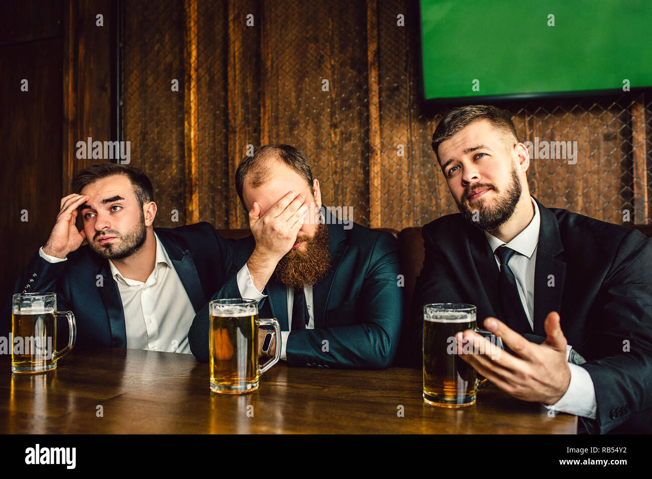 Three young office workers in suits sit at table in bar. They watch  football game. Guy on middle cover face with hand. They all are emotional  Stock Photo - Alamy