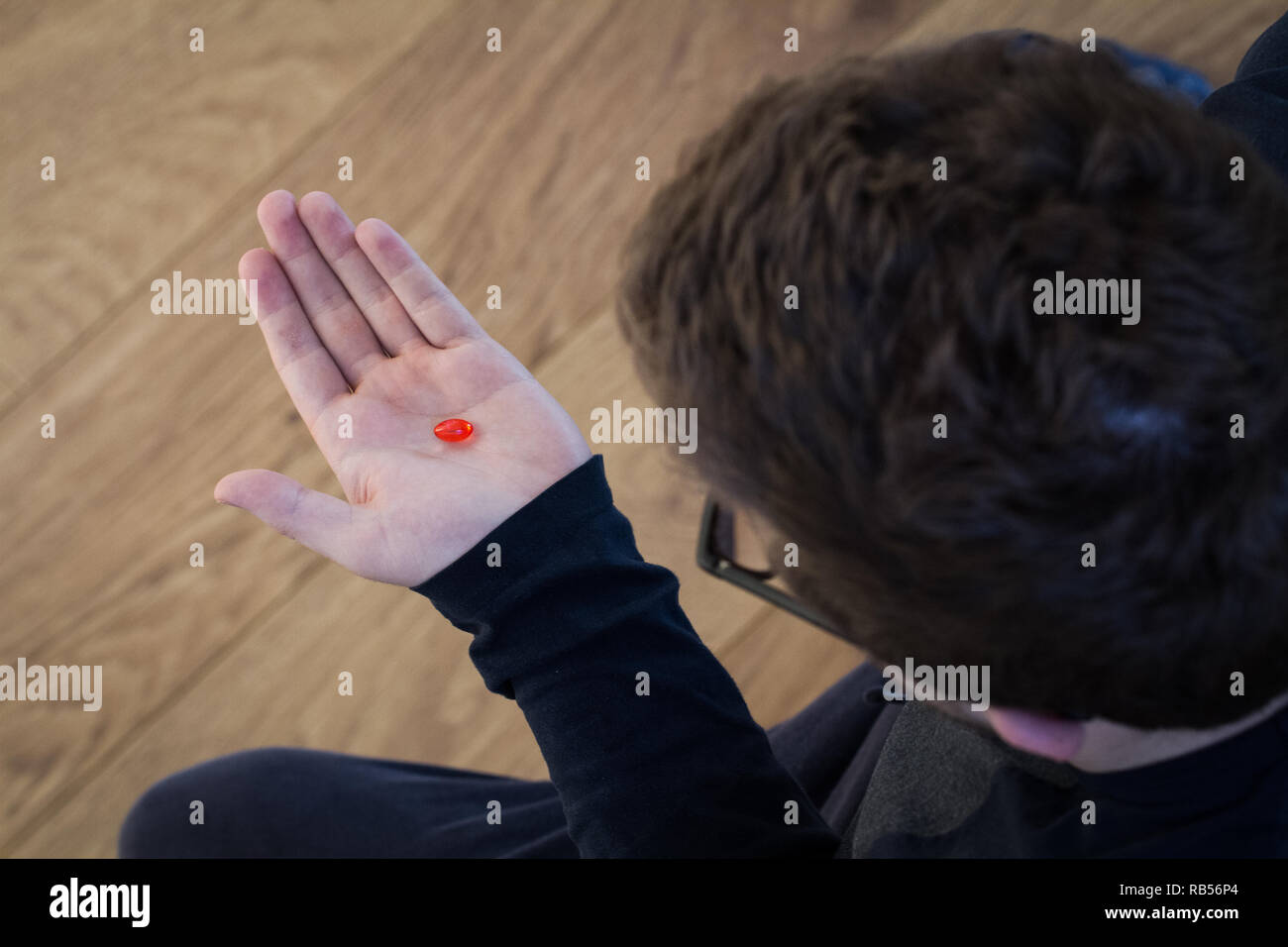 A teenage boy holding a red pill or drug in his hand before taking the medication Stock Photo