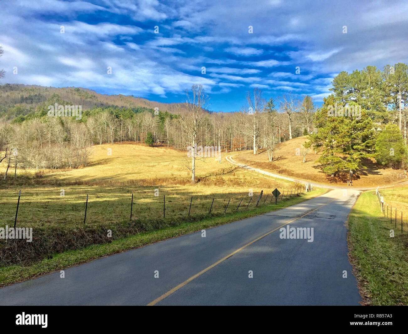 Scenic rural road with pasture, mountains, and clouds, on a peaceful winter morning. Shadows give it a secluded feeling. Stock Photo