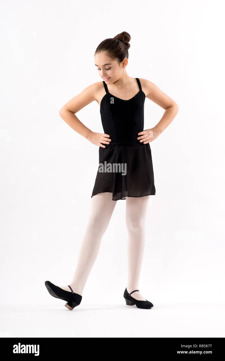 Young character ballerina in a black outfit wearing low healed court shoes standing with hands on hips looking down at her foot with a smile isolated  Stock Photo