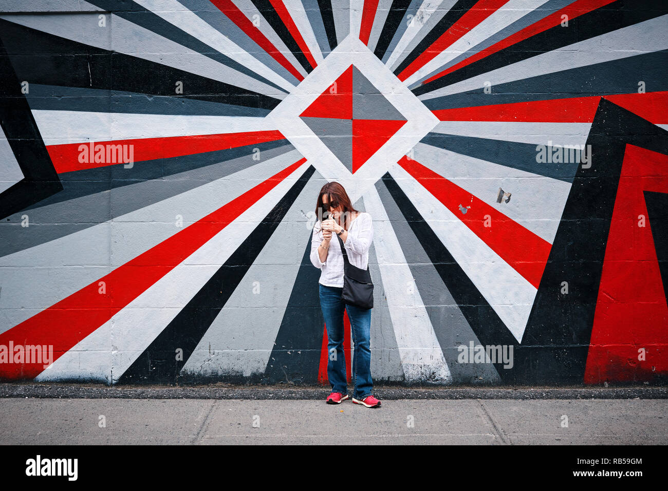 Young woman lighting her cigarette in front of a colorful graffiti wall on the street Stock Photo