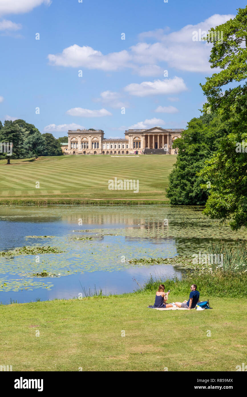 A young couple enjoying a picnic beside the lake at Stowe House Gardens, Buckinghamshire UK Stock Photo