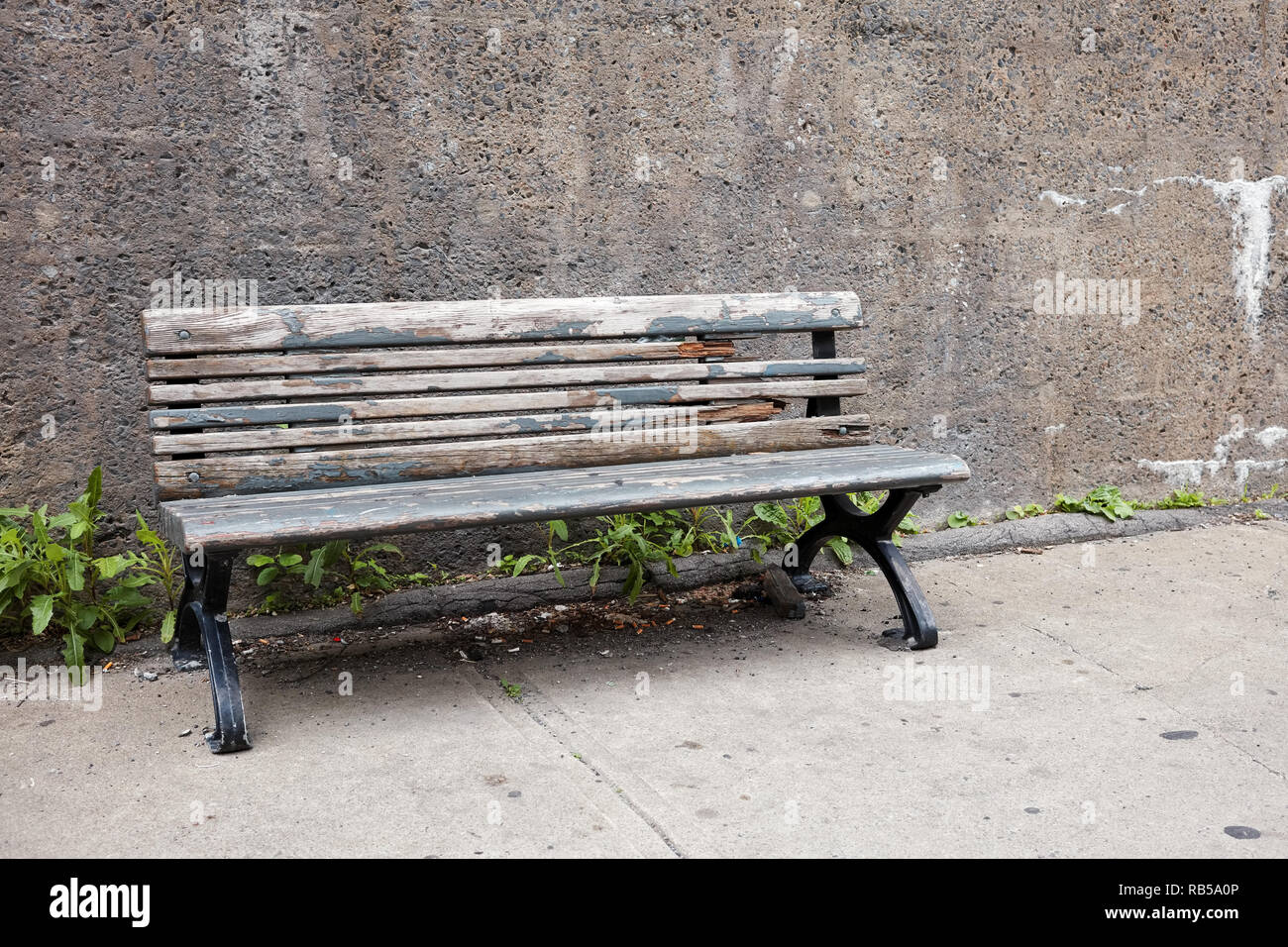 Old obsolete wooden bench on the sidewalk in front of a concrete wall ...
