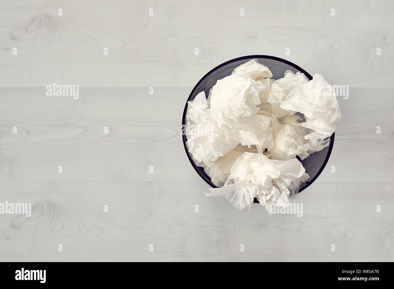 Black metal trash bin full of crumpled waste paper on white wooden