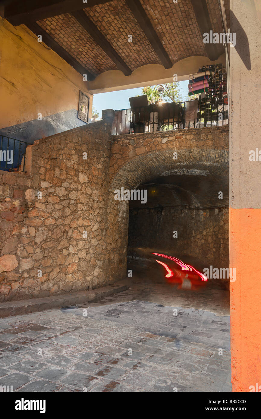 Red car entering Guanajuato underground tunnel, with walkway above