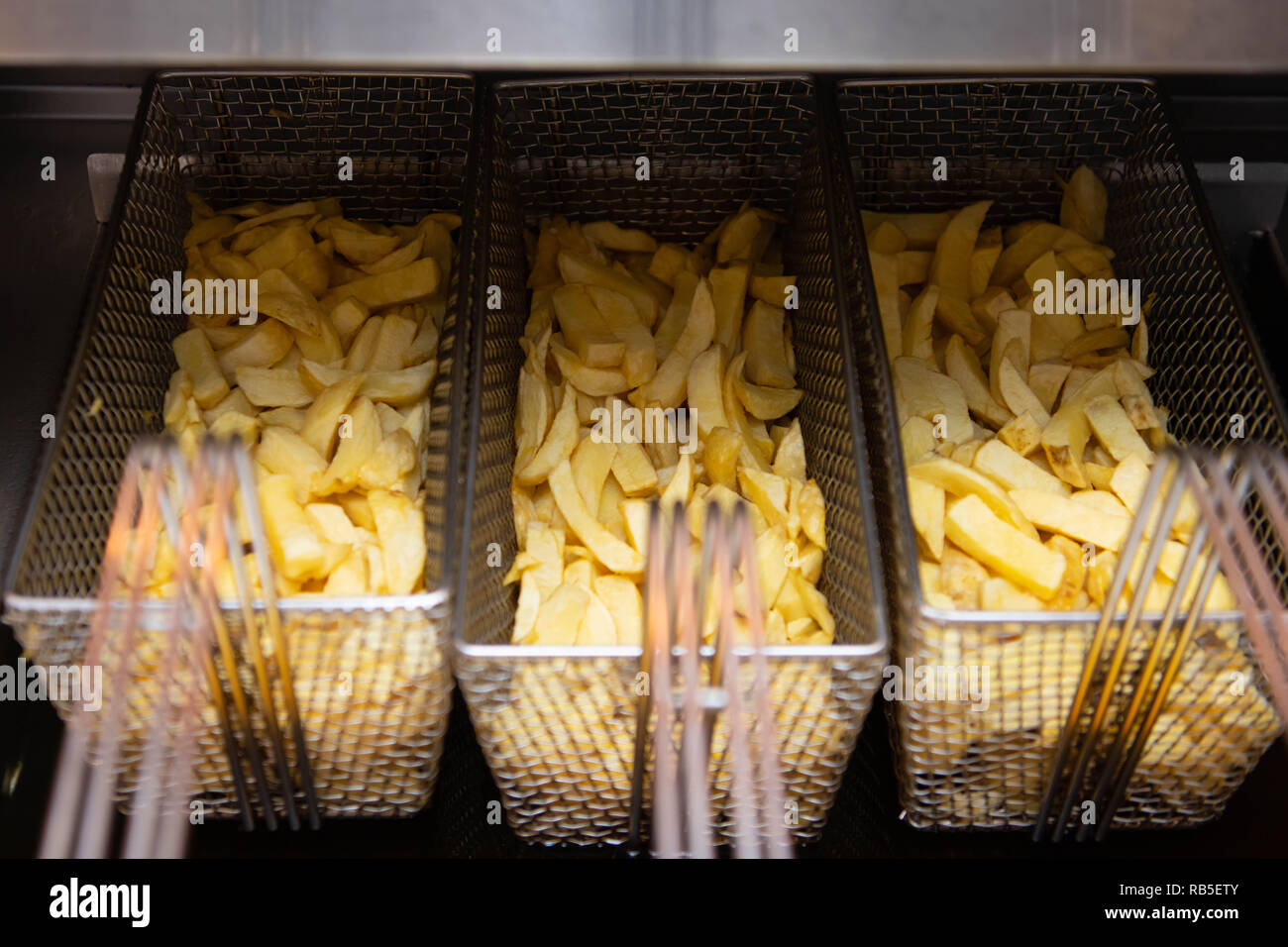 Potato chips ready to cook in a deep fat fryer in a chip shop in the UK