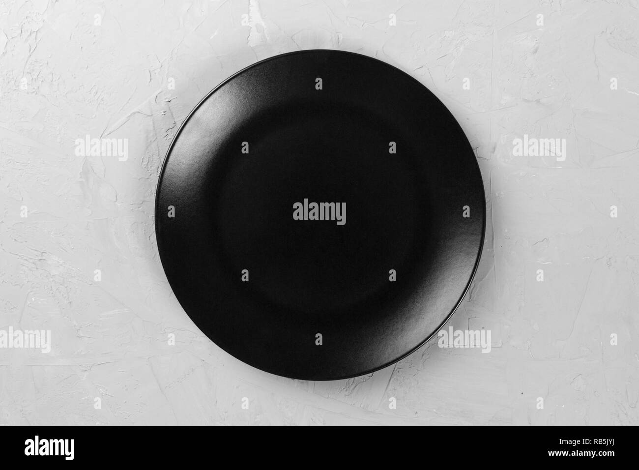 Top view of matte round empty dark dish on grey cement background space ...