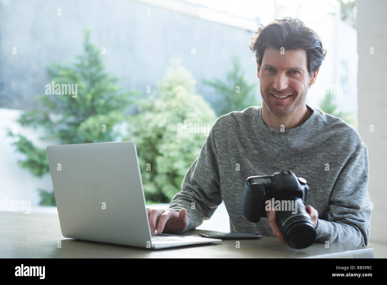 Man using laptop and holding digital camera Stock Photo