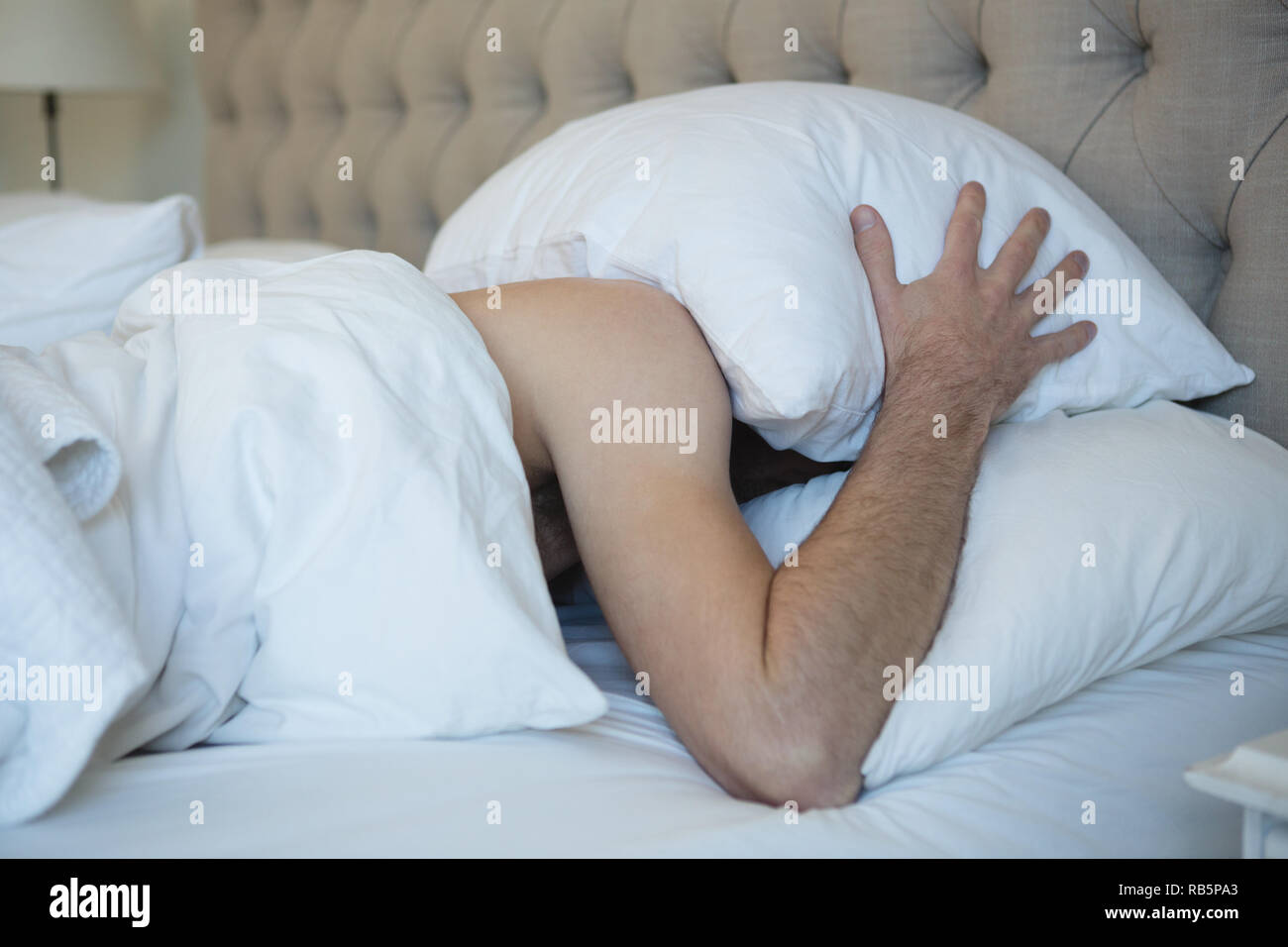Man with pillow covering his face while sleeping in bedroom Stock Photo