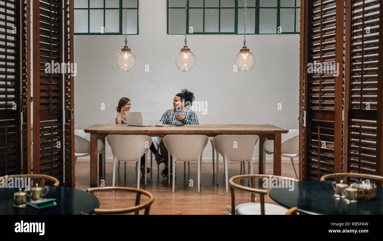 Two young creatives having a meeting in private boardroom in a cafe with laptop Stock Photo