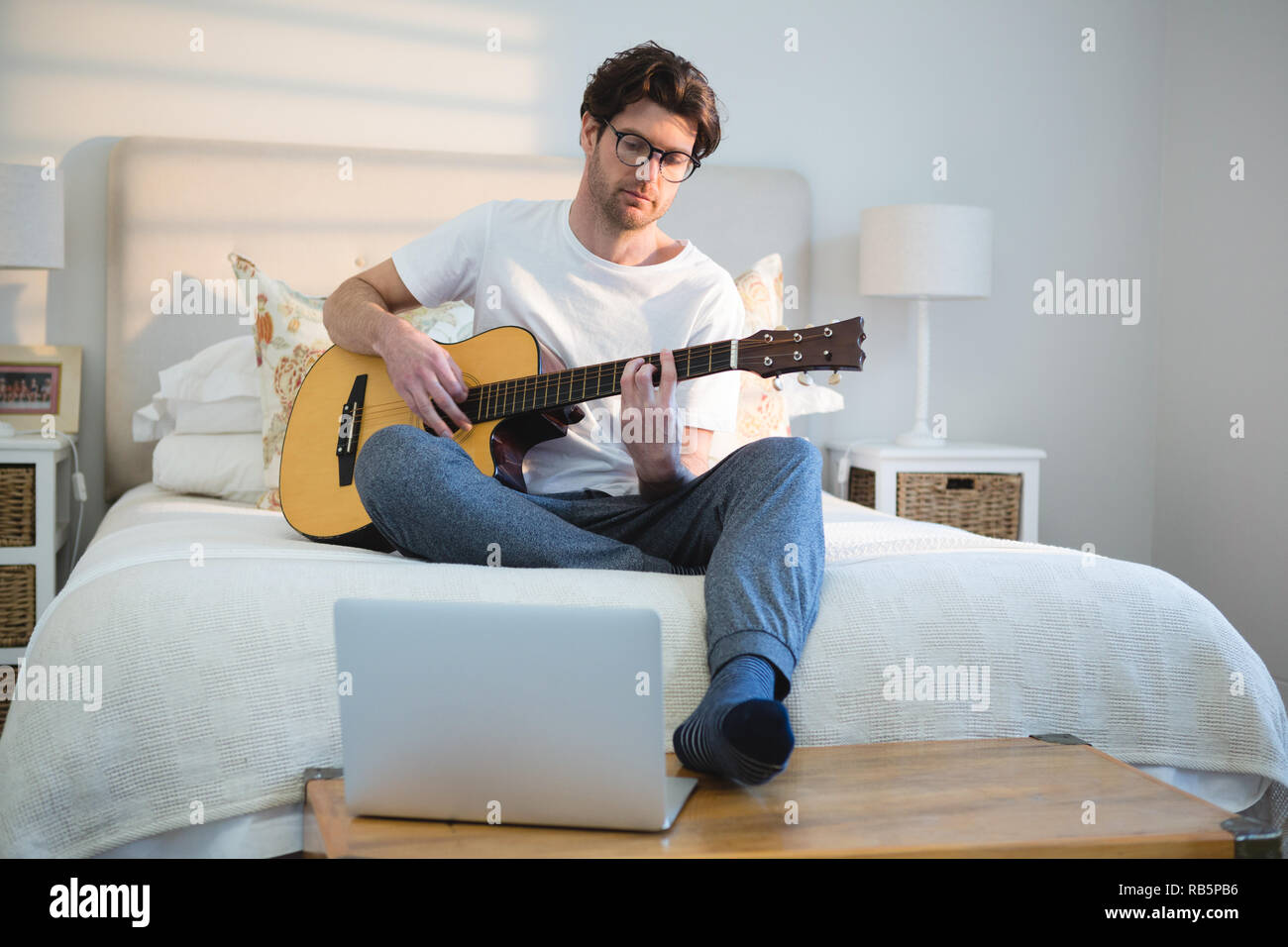 Man playing guitar in bedroom Stock Photo