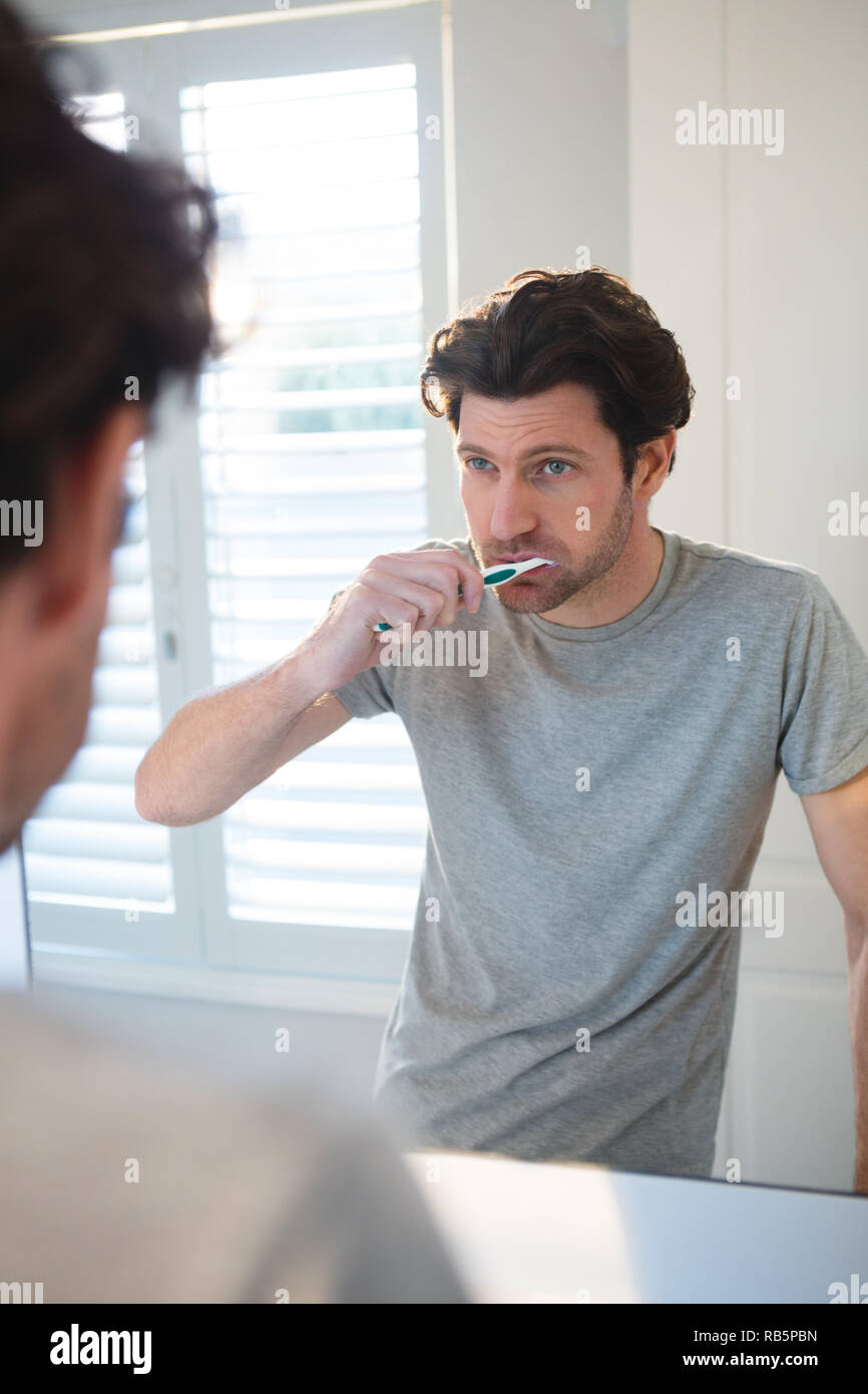 Man looking at mirror and brushing his teeth in bathroom Stock Photo