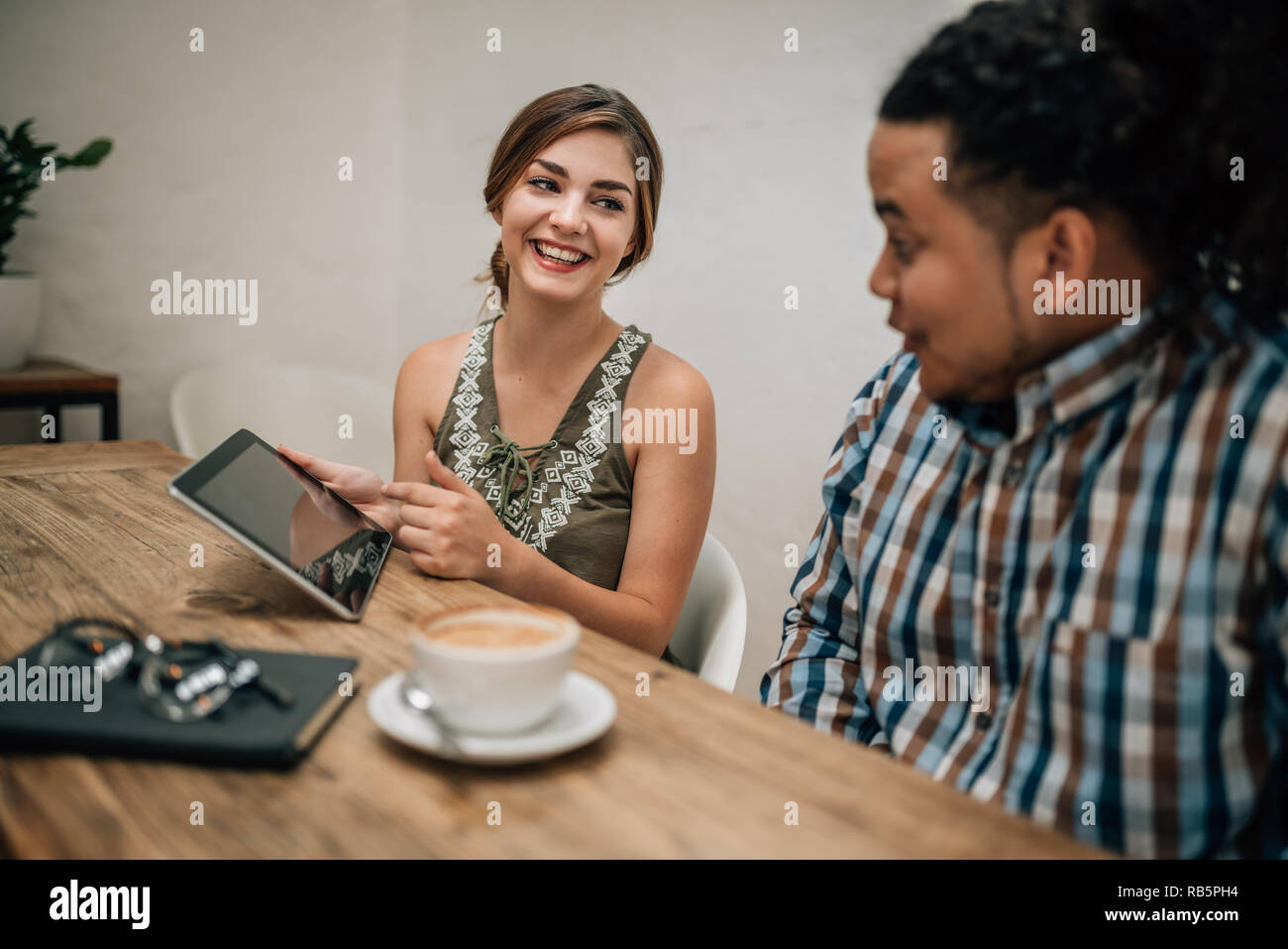 Two young creatives talking and laughing, using tablet in boardroom Stock Photo