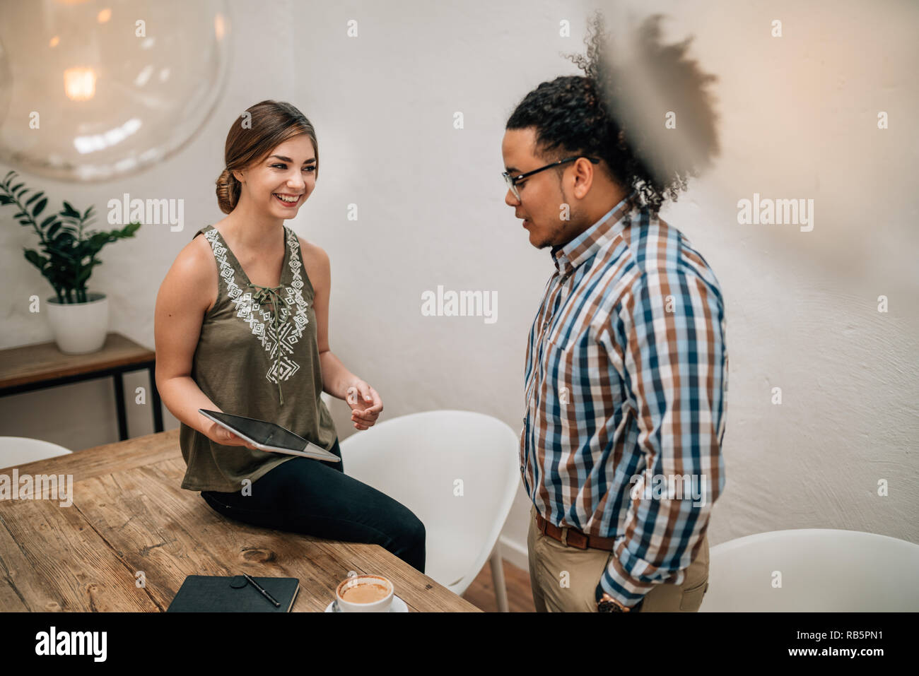 Two young creatives talking and laughing, using tablet in boardroom Stock Photo