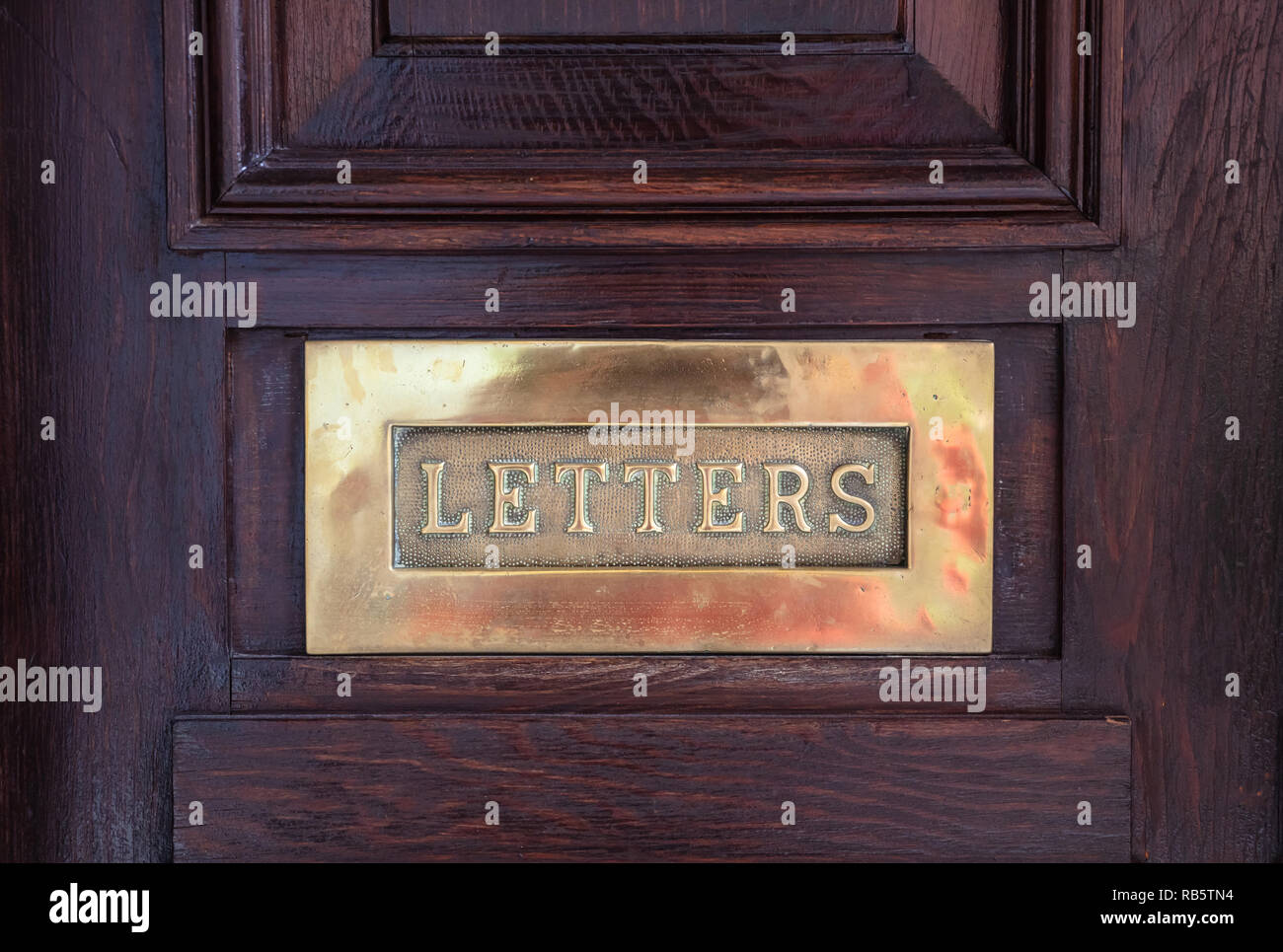 Bronze mailbox. Brass letterbox plate on a wooden front door, text letters. Closeup view with details Stock Photo