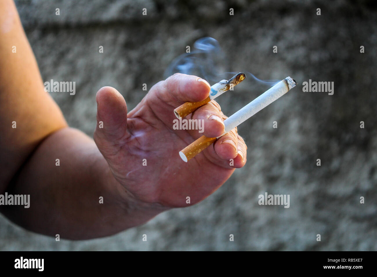 Human hand holding two cigarettes burning at the same time Stock Photo