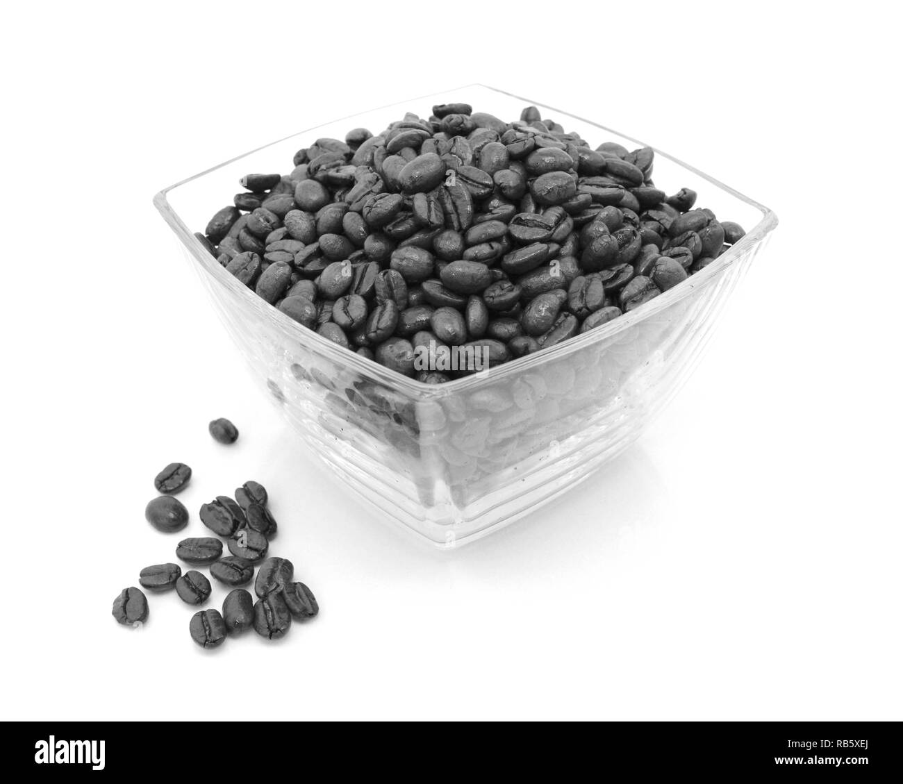 Glass dish filled with roasted coffee beans with some spilled beside on a white background - monochrome processing Stock Photo