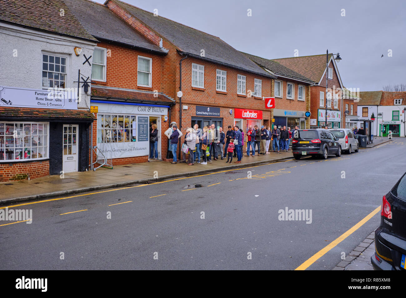 A long queue of people on the pavement waiting to enter the local butchers shop near Christmas in Thatcham high street, Berkshire, UK Stock Photo