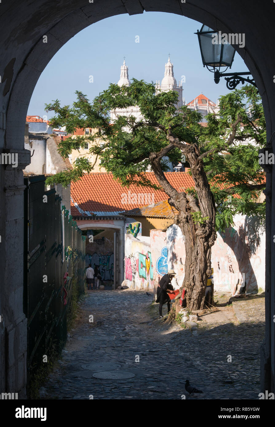 Lisbon, Portugal - May 27th 2018: Street artist under a tree with St. Vincent church in background photographed out of tunnel Stock Photo