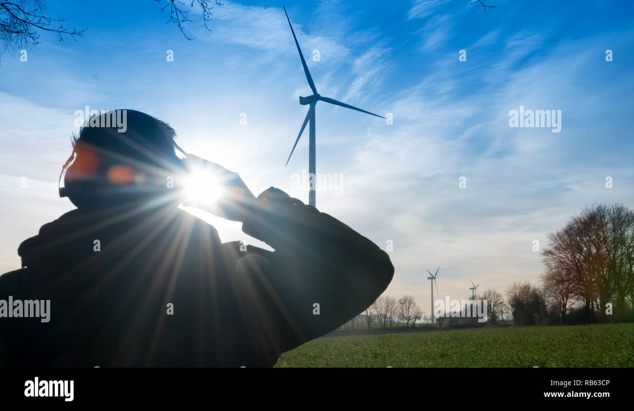 Man infront of a wind farm uses noise protector to reduce the noise of the wind turbine Stock Photo