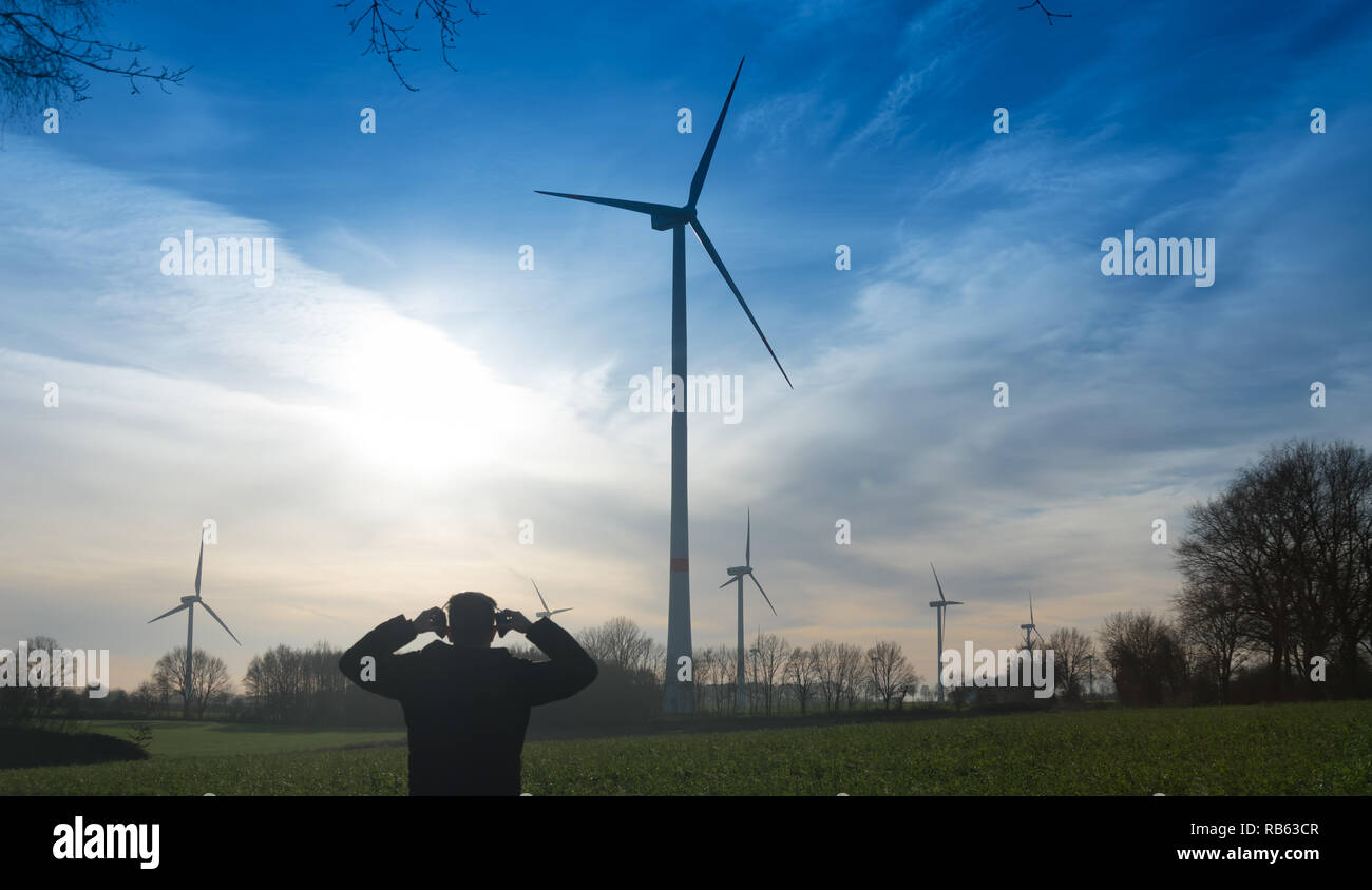 Man infront of a wind farm uses noise protector to reduce the noise of the wind turbine Stock Photo