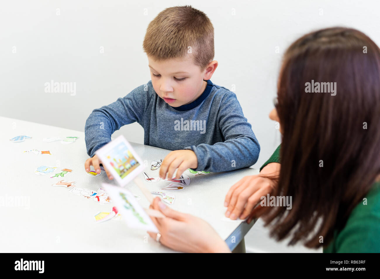Young boy in speech therapy office. Preschooler exercising correct pronunciation with speech therapist. Child Occupational Therapy Session. Stock Photo
