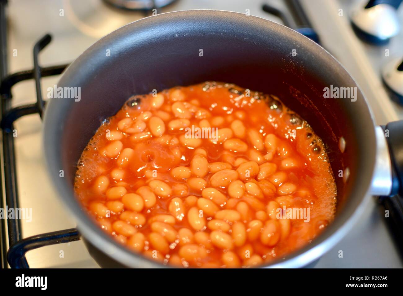 Cooking baked beans in a sauce pan on a gas hob Stock Photo