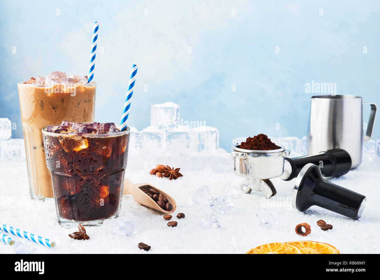 Summer drink iced coffee in a glass and ice coffee with cream in a tall glass surrounded by ice, coffee beans, portafilter, tamper, milk jug and vario Stock Photo