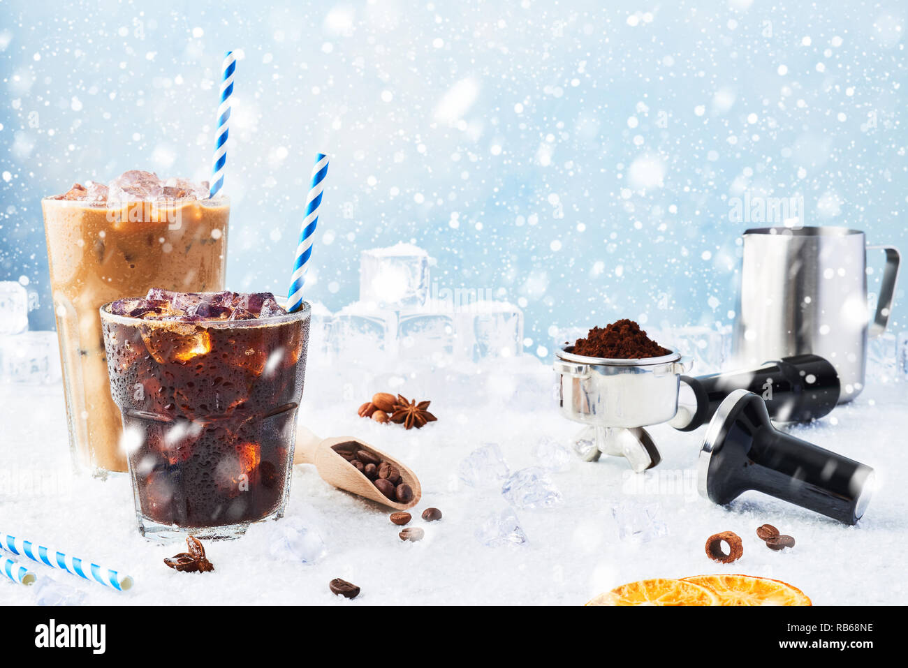 Winter drink iced coffee in a glass and ice coffee with cream in a tall glass surrounded by ice, coffee beans, portafilter, tamper, milk jug and vario Stock Photo