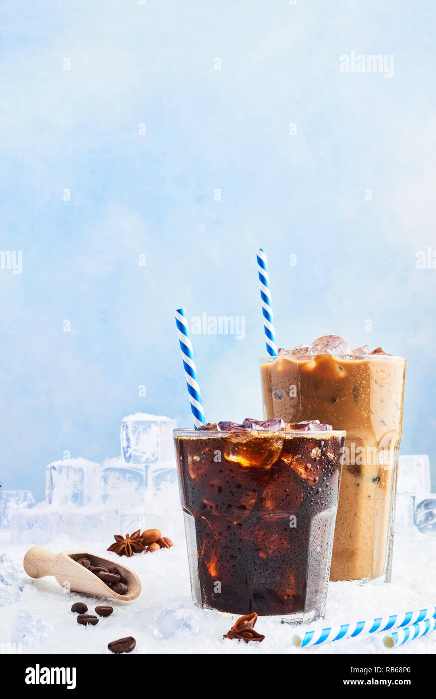 Summer drink iced coffee or soda in a glass and ice coffee with cream in a tall glass surrounded by ice cubes, coffee beans and various spices on snow Stock Photo
