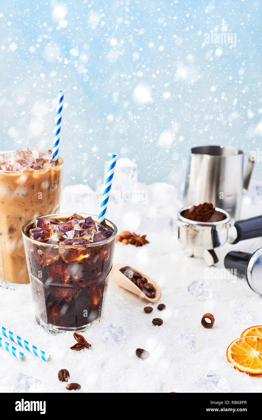 Winter drink iced coffee in a glass and ice coffee with cream in a tall glass surrounded by ice, coffee beans, portafilter, tamper, milk jug and vario Stock Photo